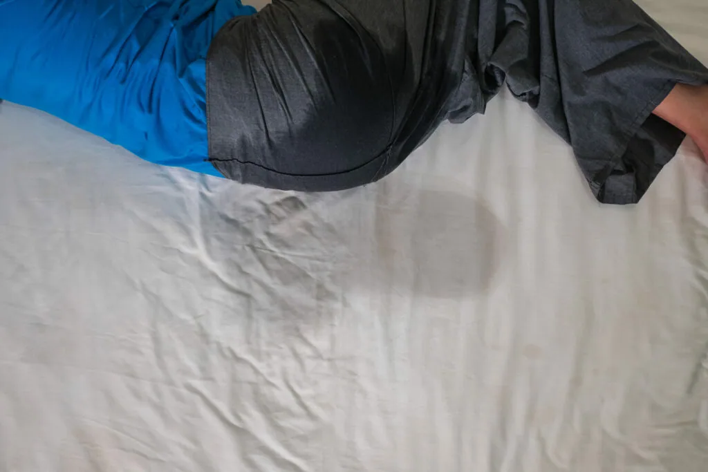 Person lying on white sheet wearing blue and dark clothing during examination