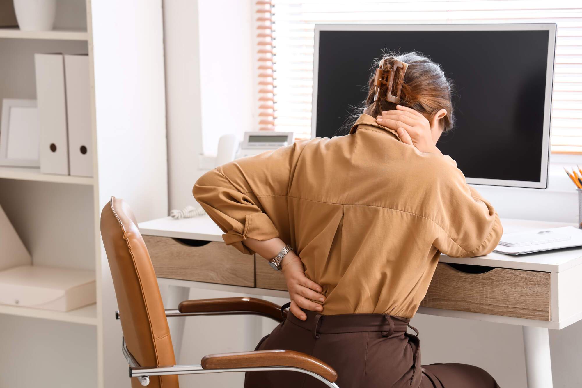 Woman sitting at desk holding her lower back in pain while working at a computer